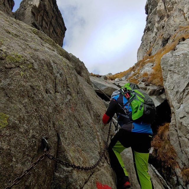 Escursionista arrampicato su parete rocciosa con casco e imbrago